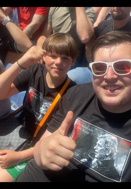 Twee jongens poseren met een duim omhoog, beiden in zwarte T-shirts met een afbeelding.