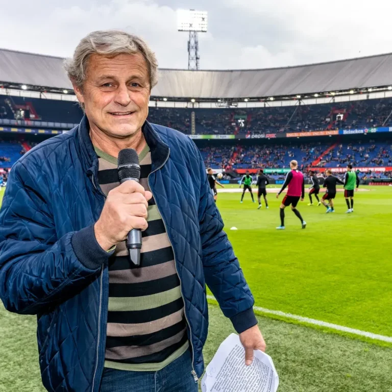 Man met microfoon in stadion, met spelers die zich voorbereiden op een wedstrijd.