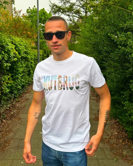 Jonge man in een wit T-shirt met opdruk, staande op een pad omgeven door groen.