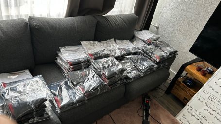 Gestapelde, plastic verpakte kledingstukken op een bank in een woonkamer.