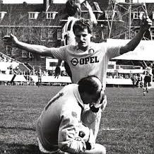 Peter Houtman viert een doelpunt met gebaren, terwijl een andere speler op de grond zit.