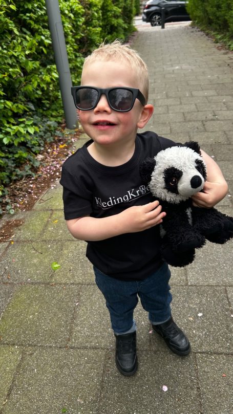 Jongen met zonnebril houdt een panda-knuffel vast op een stoep.