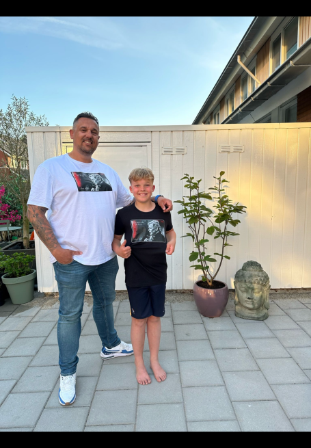 Vader en zoon poseren buiten, beiden in t-shirts met dezelfde afbeelding.