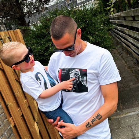 Vader houdt een kind vast, beiden dragen zonnebrillen en witte T-shirts.