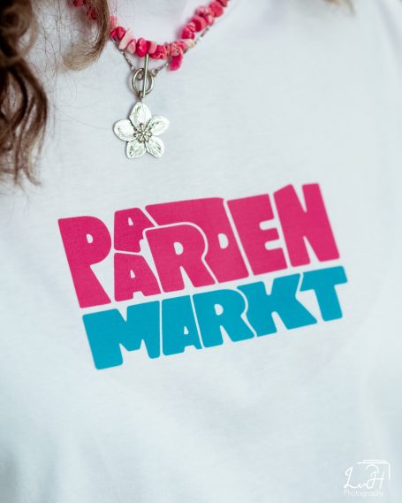 T-shirt met de tekst "PARADENMARKT" in roze en blauwe letters.