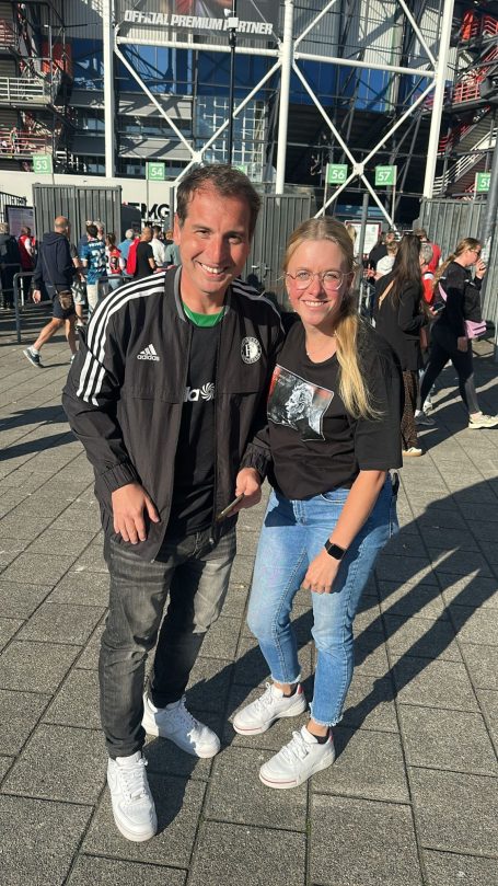 Man en vrouw poseren samen buiten een stadion, beide in sportieve kleding.