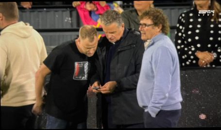Drie mannen in casual kleding kijken naar een smartphone op een evenement.